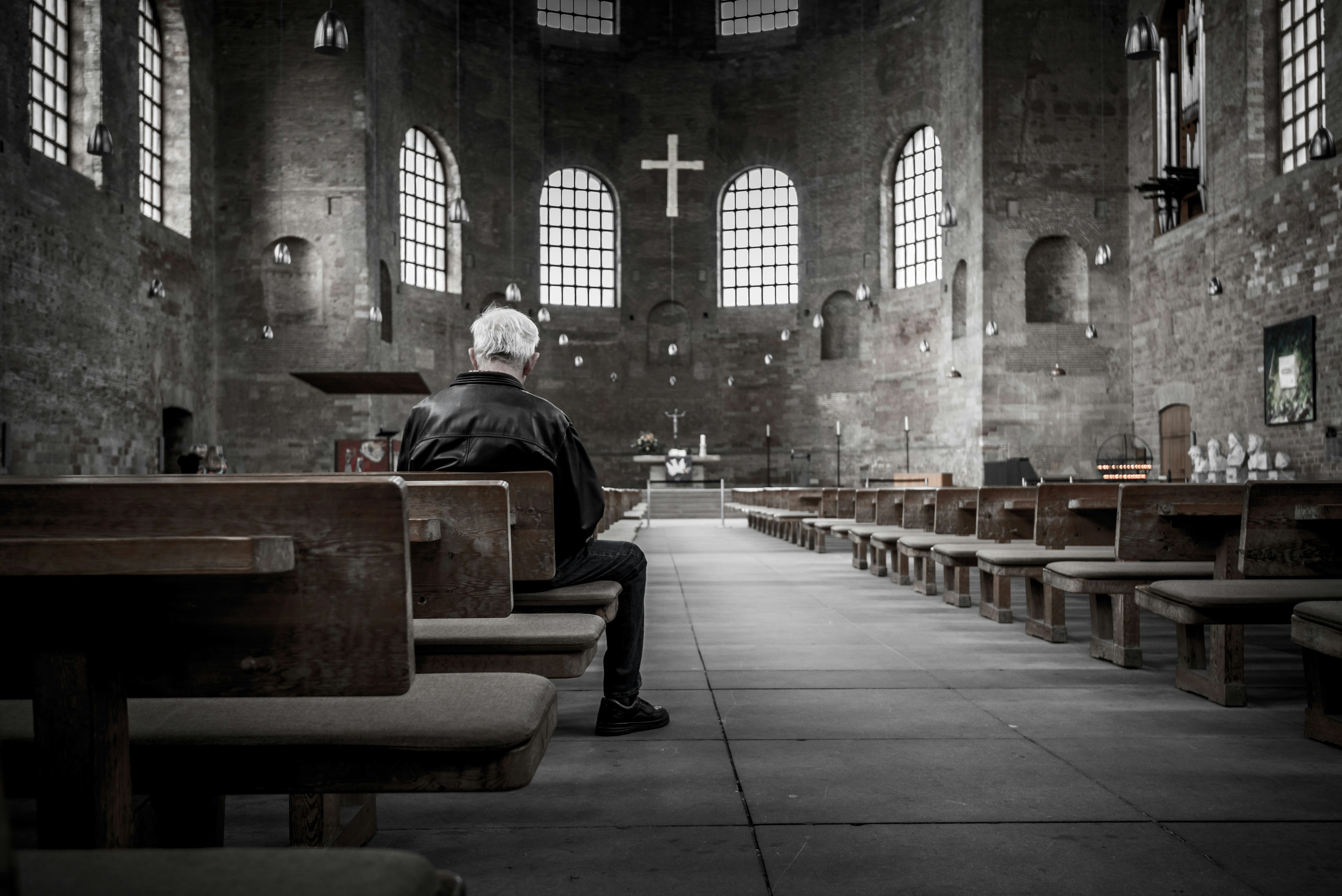 A man sitting in a church looking toward the cross in black and white